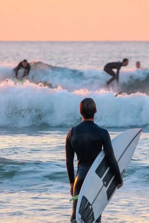 Surfer holding a surfboard while watching waves during sunset at the beach